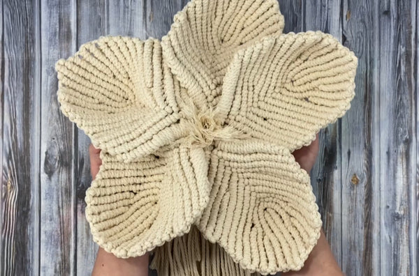 womans hands holding large macrame flower on a wood backdrop