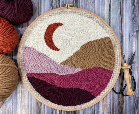 finished moon landscape punch needle wall hanging with punch needle and yarn nearby