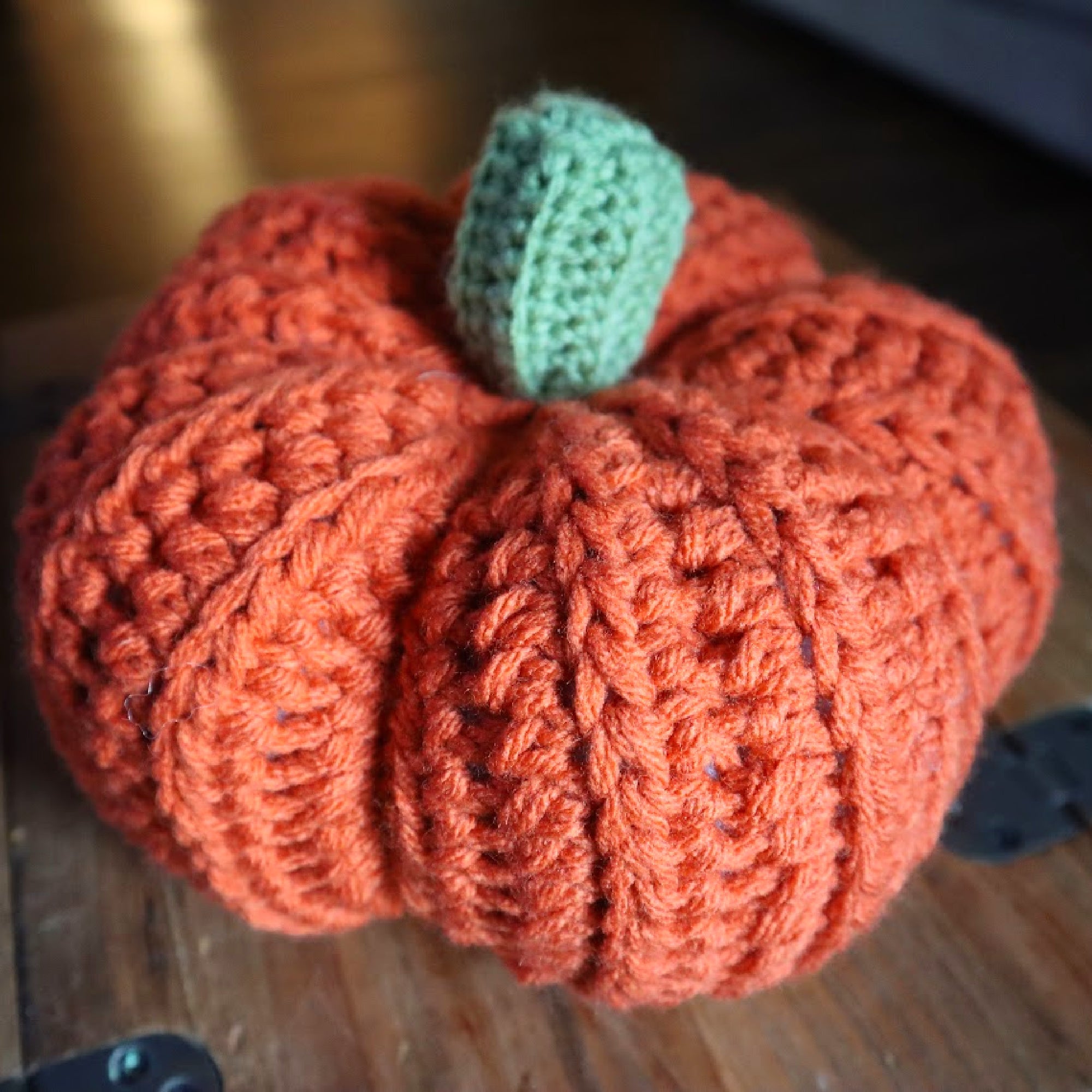 orange crochet pumpkin with a green stem on a wooden table