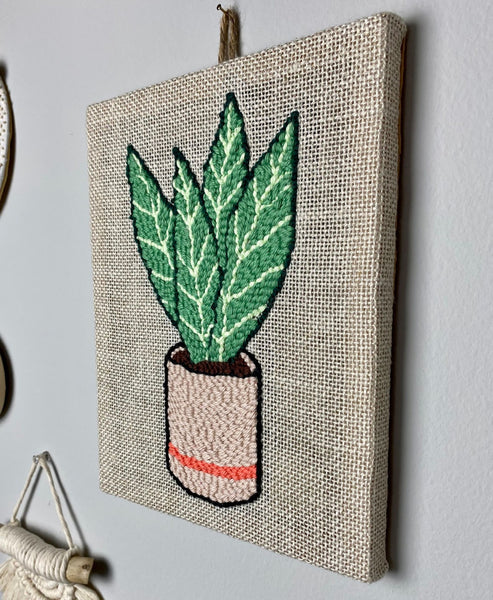 finished punch needle snake plant wall hanging on a light gray wall
