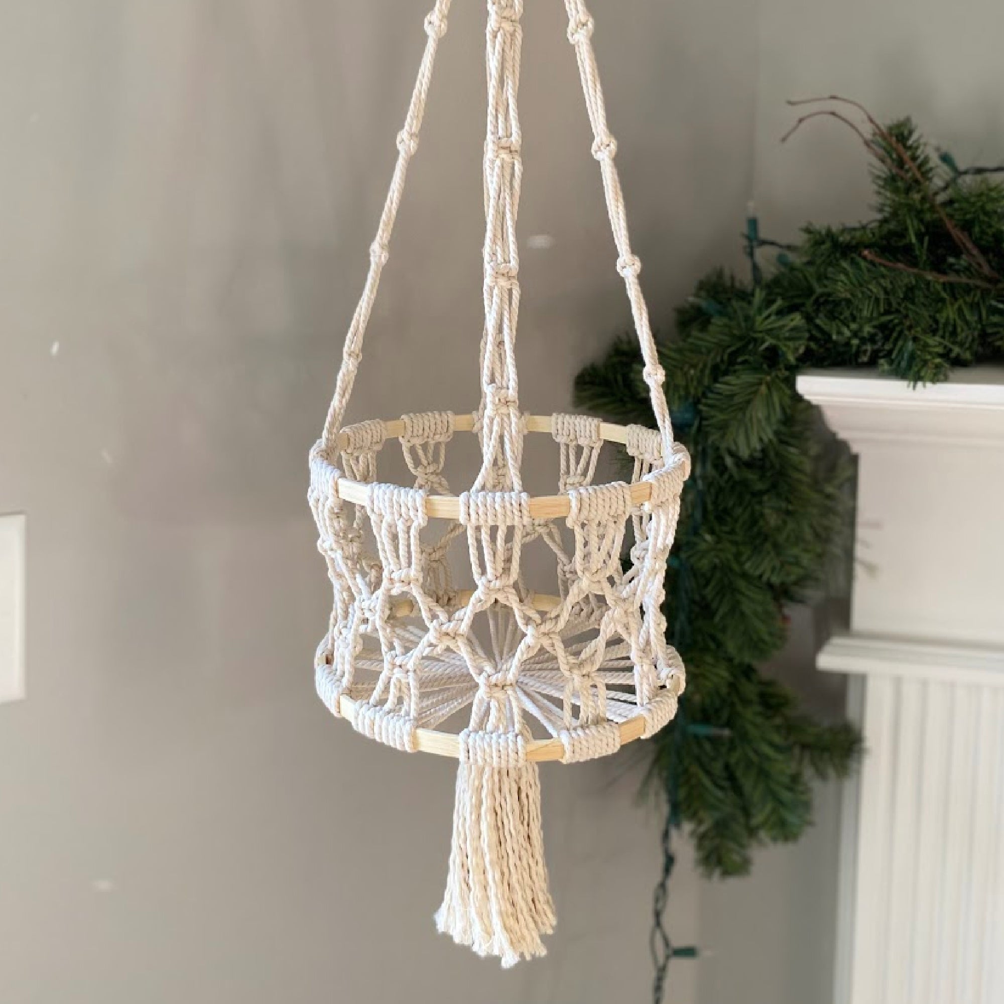 finished macrame hanging basket in front of a gray wall and greenery in the background