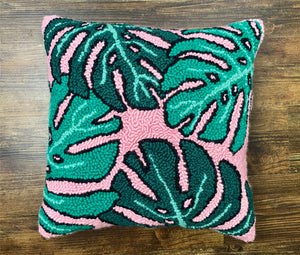 finished monstera punch needle pillow laying on a wooden surface